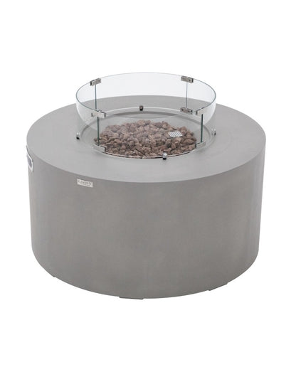 Elementi Pacaya Round Hidden Propane Tank Fire Pit Table in light grey GFRC concrete, showcasing rustic lava rocks and a protective glass wind guard. This elegantly designed fire feature blends durability with modern aesthetics, making it a perfect centerpiece for outdoor ambiance and warmth.