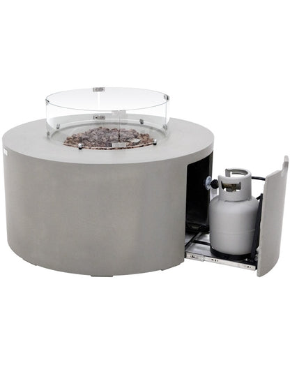 "Elementi Pacaya Round Hidden Propane Tank Fire Pit Table in light grey GFRC concrete, featuring a sleek glass wind guard, rustic lava rocks, and a seamlessly integrated pull-out drawer for propane tank storage. This modern fire feature combines elegance, functionality, and warmth, perfect for elevating any outdoor space.
