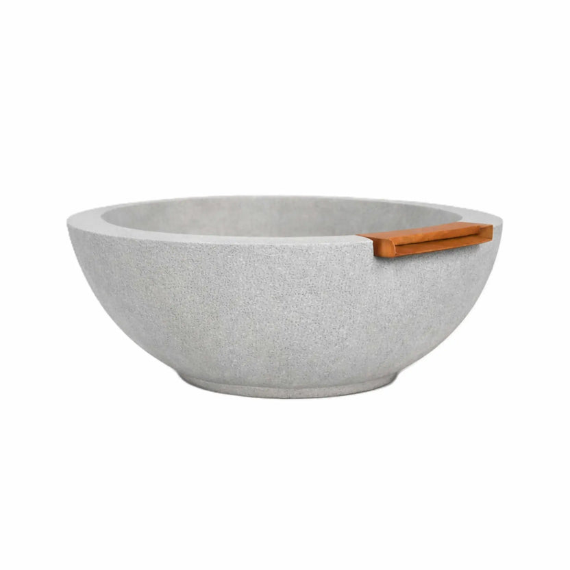 Gray round concrete fire and water bowl featuring a textured finish and built-in bronze spillway, shown without fire or water to highlight the bowl’s shape, color, and outdoor installation design.