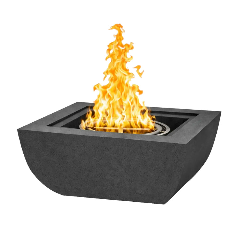 Studio product image of a Flame Havens Serenity Series square curved fire bowl in a dark graphite or black finish. The modern concrete fire bowl features smooth curved sides and a recessed burner ring producing tall yellow flames. The bowl sits against a clean white background, highlighting the minimalist design and contemporary outdoor fire feature style.