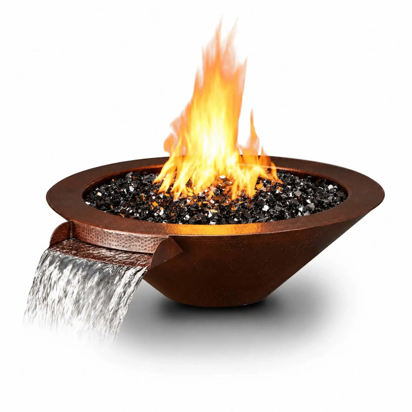 Flame Havens Bella hammered copper fire and water bowl isolated on a white background. The angled product view shows a wide circular rim, tapered copper body, and glossy black fire glass with tall yellow-orange flames. Water cascades from the copper scupper at the front left, with a soft shadow beneath the bowl.