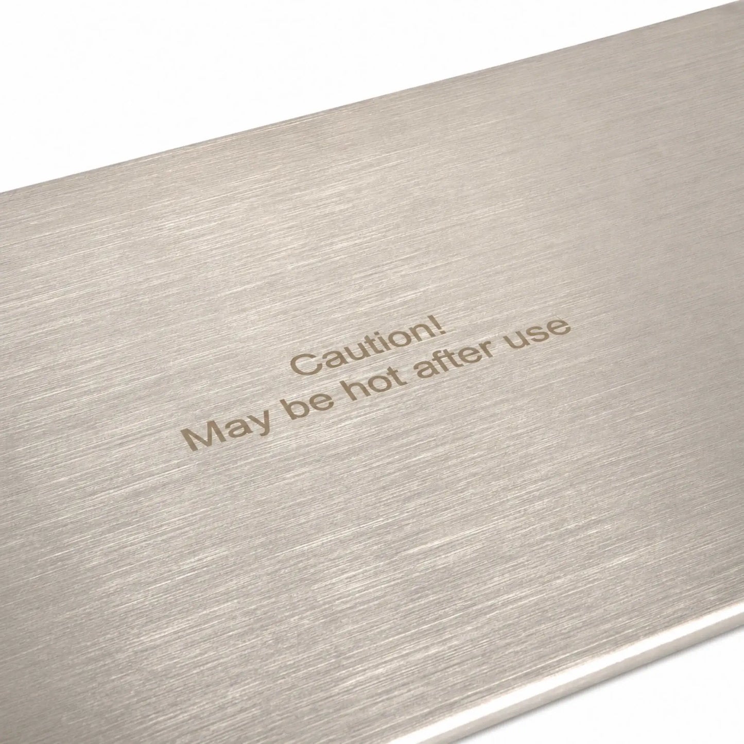 Close-up of the Flame Havens Refuge Series 33 x 11-inch stainless steel rectangular burner cover, highlighting its brushed metal grain and engraved safety message reading, “Caution! May be hot after use.” The detailed view shows the cover’s clean finish and clearly visible heat-warning label.