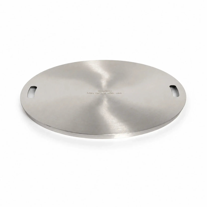 Main view of the Flame Havens Refuge Series 24-inch round stainless steel burner cover. Shown at a low angle on a white background, the circular accessory features a reflective brushed finish, two integrated handle openings, a slim raised edge, and the engraved message, “Caution! May be hot after use.”