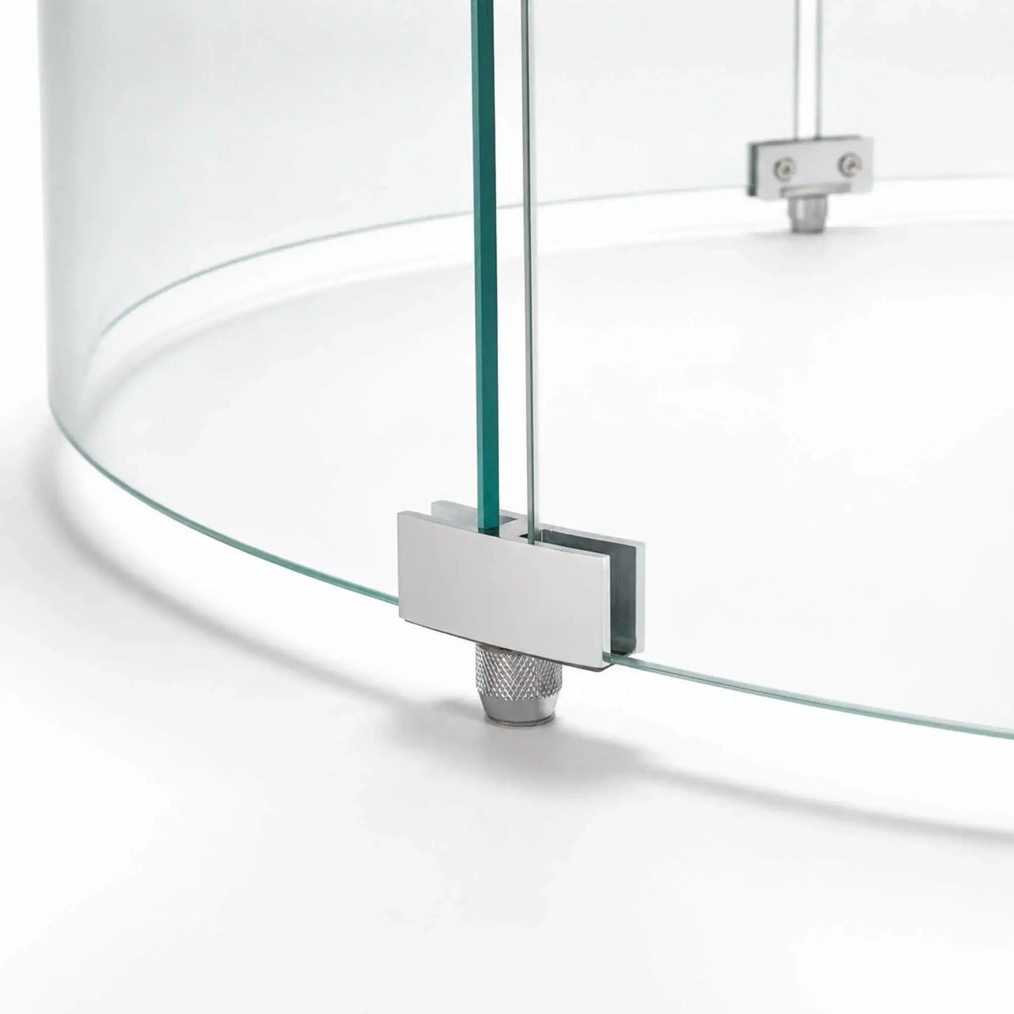 Close-up of a support foot on the Flame Havens Refuge Series 28-inch round by 7-inch-tall tempered glass wind guard shield. The silver metal bracket secures two curved glass panels while a knurled adjustable foot supports the assembly above the fire pit surface.