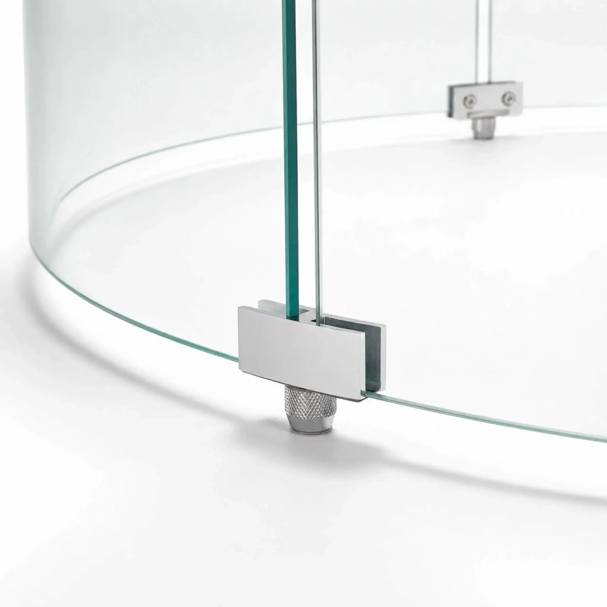 Close-up of a support foot on the Flame Havens Refuge Series 28-inch round by 7-inch-tall tempered glass wind guard shield. The silver metal bracket secures two curved glass panels while a knurled adjustable foot supports the assembly above the fire pit surface.