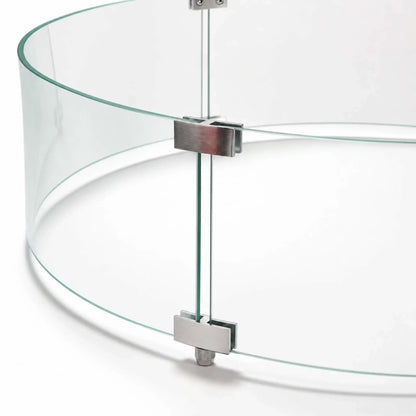 Close-up of the hardware joining the curved panels of the Flame Havens Refuge Series 28-inch round by 7-inch-tall tempered glass wind guard shield. Silver upper and lower clamps align the clear glass edges, with screws and an adjustable support foot visible against a white background.