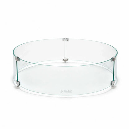 Front main view of the Flame Havens Refuge Series 28-inch round by 7-inch-tall tempered glass wind guard shield. The clear circular enclosure features green-tinted glass edges, silver panel connectors, three raised support feet, and visible hot-surface caution markings along the lower panels.