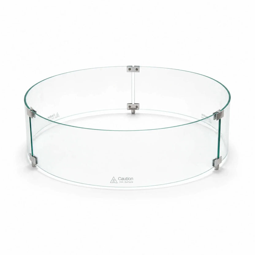 Angled main view of the assembled Flame Havens Refuge Series tempered glass wind guard shield, measuring 28 inches in diameter by 7 inches tall. Three curved clear glass panels form a complete circle, joined by silver clamps and raised support feet, with “Caution Hot Surface” warnings near the bottom.