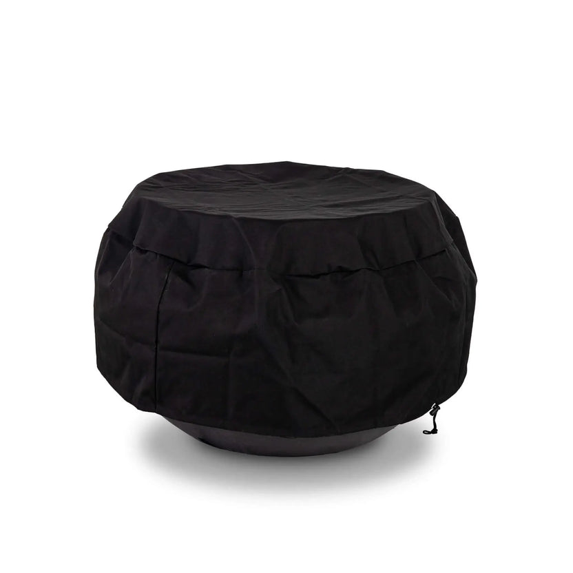 The Flame Havens Refuge Series 36-inch Round Natural Gas GFRC Concrete Fire Pit in Black protected by the black canvas fabric cover while installed over the optional tempered glass wind guard. The fitted weather-resistant cover accommodates the wind guard, providing year-round protection for premium outdoor fire pit accessories without requiring removal.