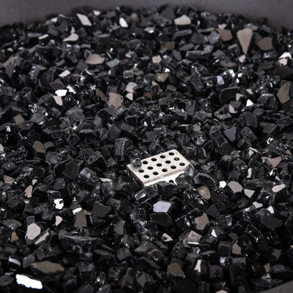 Detailed close-up of the Flame Havens Refuge Series 36-inch Round Natural Gas GFRC Concrete Fire Pit featuring premium black reflective fire glass surrounding the stainless steel CSA ignition assembly. The image emphasizes the glass texture, reflective finish, and clean installation that enhances both daytime appearance and nighttime flame presentation.