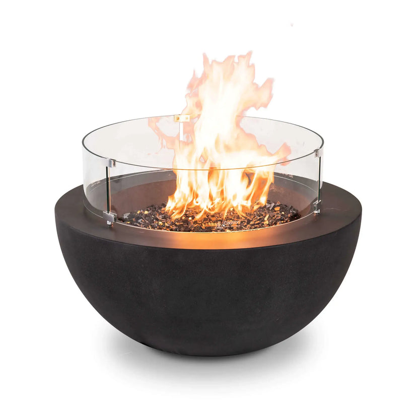 Front product image of the Flame Havens Refuge Series 36-inch Round Natural Gas GFRC Concrete Fire Pit in Black operating with premium tempered black reflective fire glass and the optional tempered glass wind guard installed. Bright natural gas flames rise above the reflective fire media while the clear wind guard enhances safety and flame stability without obstructing the modern round GFRC concrete design.
