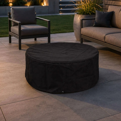 Lifestyle image of the Flame Havens Refuge Series 36-inch Round Natural Gas Gray GFRC Concrete Fire Pit covered with the custom black canvas fabric cover on a luxury backyard patio. Positioned between modern outdoor seating, the weatherproof cover protects the fire pit while complementing upscale outdoor living spaces during the off-season or between uses.