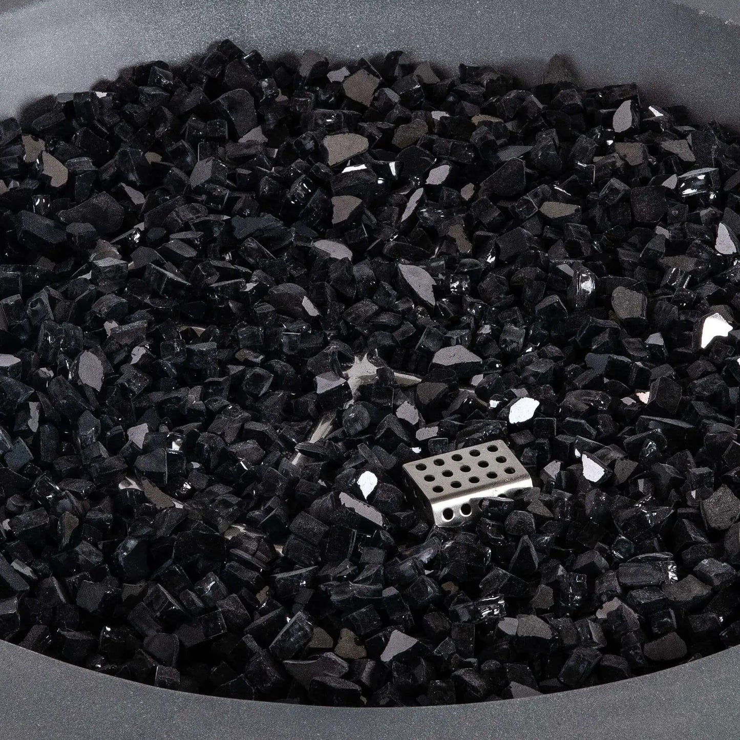 Close-up of premium black reflective fire glass inside the Flame Havens Refuge Series 36-inch Round Natural Gas Gray GFRC Concrete Fire Pit. The image highlights the angular tempered glass media, reflective finish, and partially concealed CSA ignition burner, demonstrating the elegant appearance and premium quality of the fire feature components.
