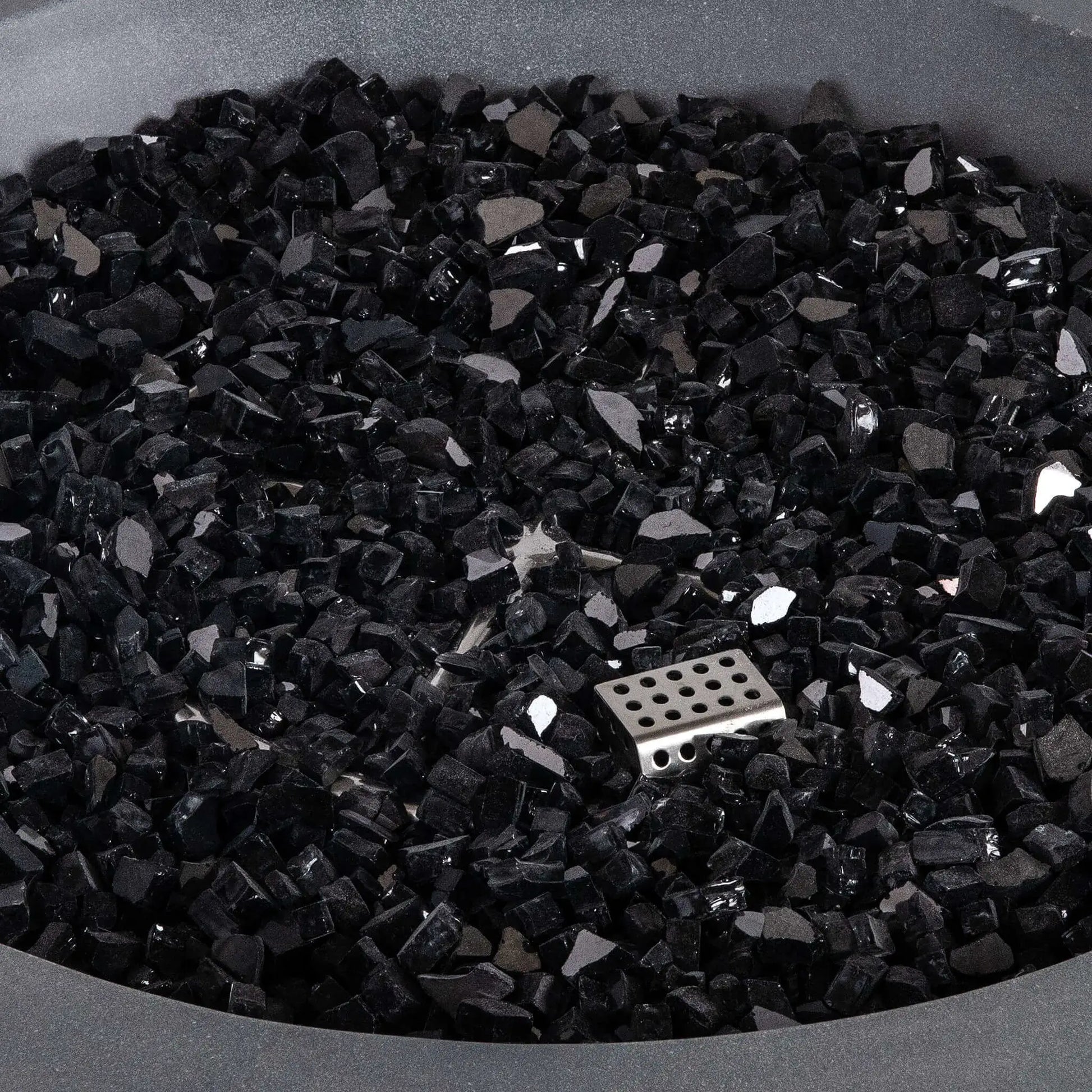 Close-up of premium black reflective fire glass inside the Flame Havens Refuge Series 36-inch Round Natural Gas Gray GFRC Concrete Fire Pit. The image highlights the angular tempered glass media, reflective finish, and partially concealed CSA ignition burner, demonstrating the elegant appearance and premium quality of the fire feature components.
