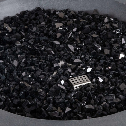Close-up of premium black reflective fire glass inside the Flame Havens Refuge Series 36-inch Round Natural Gas Gray GFRC Concrete Fire Pit. The image highlights the angular tempered glass media, reflective finish, and partially concealed CSA ignition burner, demonstrating the elegant appearance and premium quality of the fire feature components.
