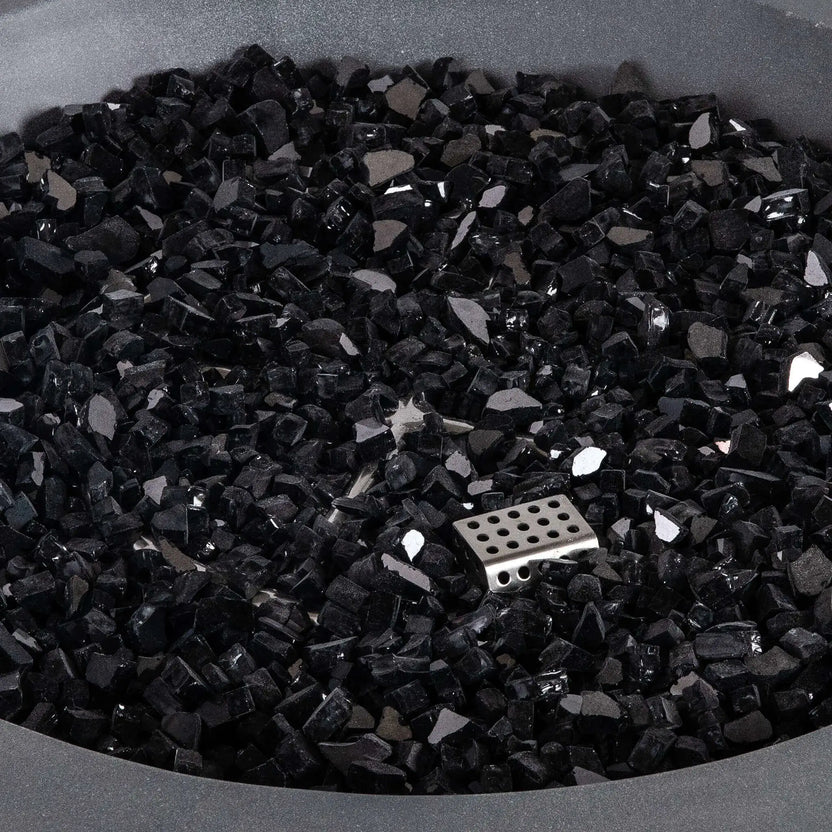 Close-up of premium black reflective fire glass inside the Flame Havens Refuge Series 36-inch Round Natural Gas Gray GFRC Concrete Fire Pit. The image highlights the angular tempered glass media, reflective finish, and partially concealed CSA ignition burner, demonstrating the elegant appearance and premium quality of the fire feature components.