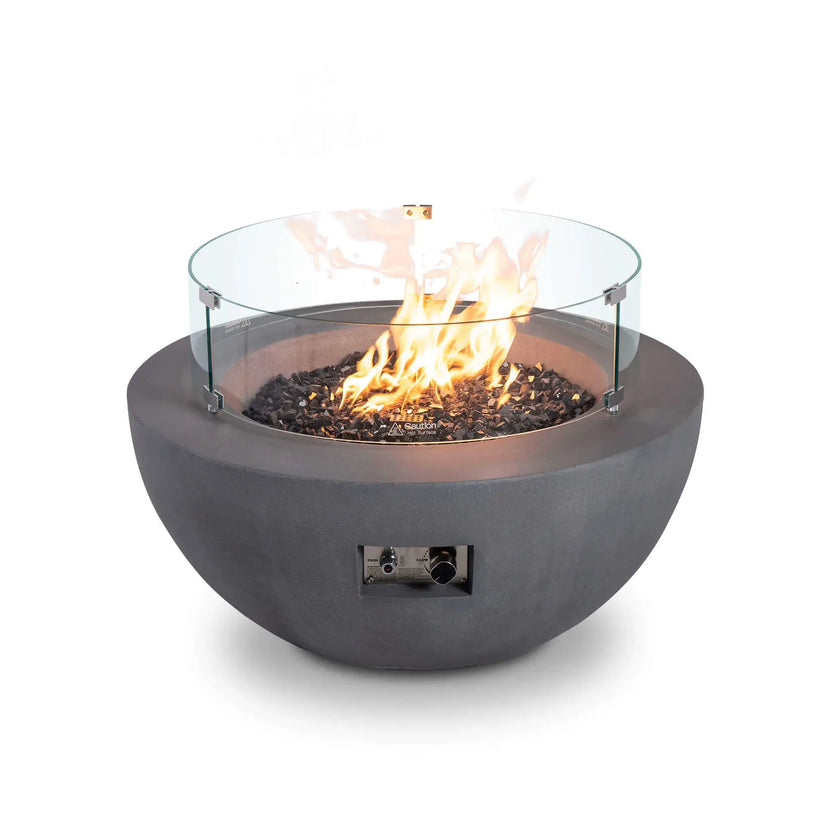 Studio image of the Flame Havens Refuge Series 36-inch Round Natural Gas GFRC Concrete Fire Pit in Gray featuring a clear tempered glass wind guard surrounding the active flame. Black tempered reflective fire glass complements the modern concrete bowl while the stainless steel burner produces a tall, even flame protected from outdoor breezes.