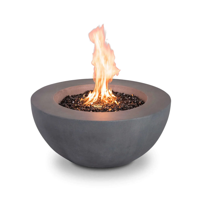 The Flame Havens Refuge Series 36-inch Round Natural Gas GFRC Concrete Fire Pit in Gray is shown with vibrant flames rising above black tempered reflective fire glass. The recessed stainless steel burner delivers an attractive vertical flame presentation while the front remains free of visible controls for a clean architectural appearance.