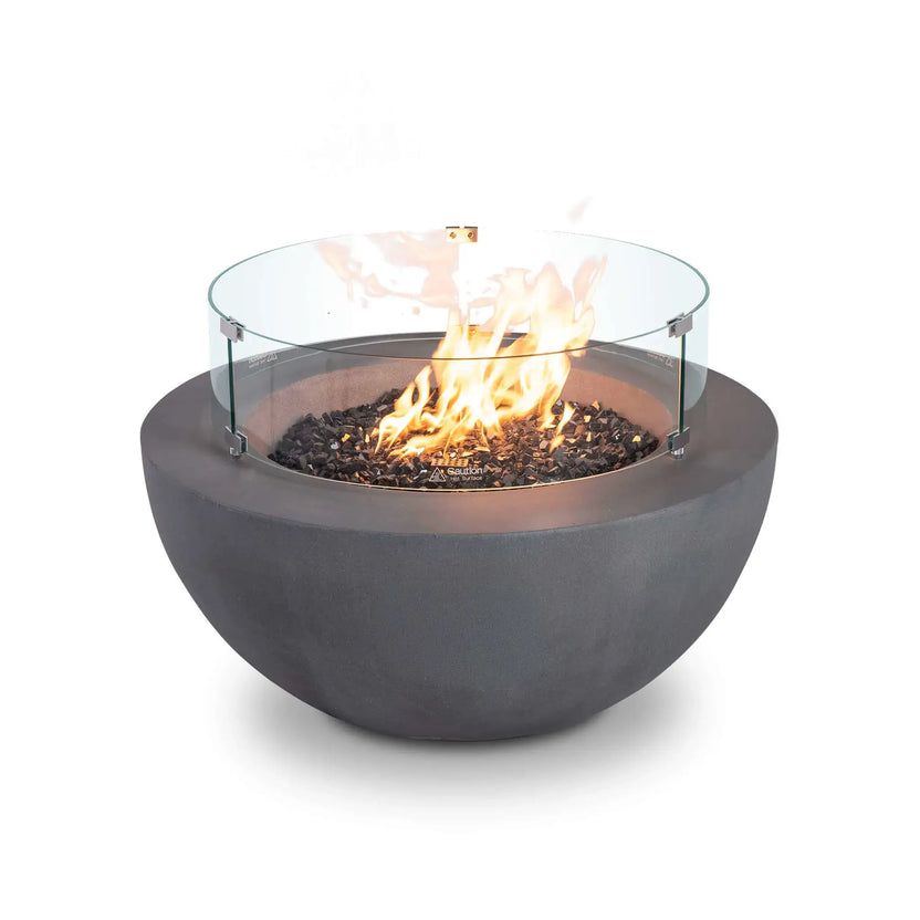 Front product image of the Flame Havens Refuge Series 36-inch Round Natural Gas GFRC Concrete Fire Pit in Gray featuring a clear tempered glass wind guard and black tempered reflective fire glass. Bright flames rise from the stainless steel burner while the low-profile gray GFRC concrete bowl creates a clean, contemporary outdoor fire feature designed for premium patios and outdoor living spaces.