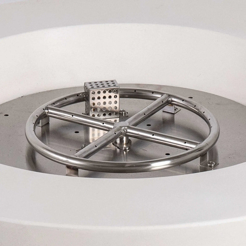 Close-up of the Flame Havens Refuge Series stainless steel burner and CSA-certified ignition assembly inside the 36-inch Round Natural Gas White GFRC Concrete Fire Pit. The precision-engineered circular burner, cross supports, and ignition housing demonstrate the premium construction designed for reliable outdoor fire performance.