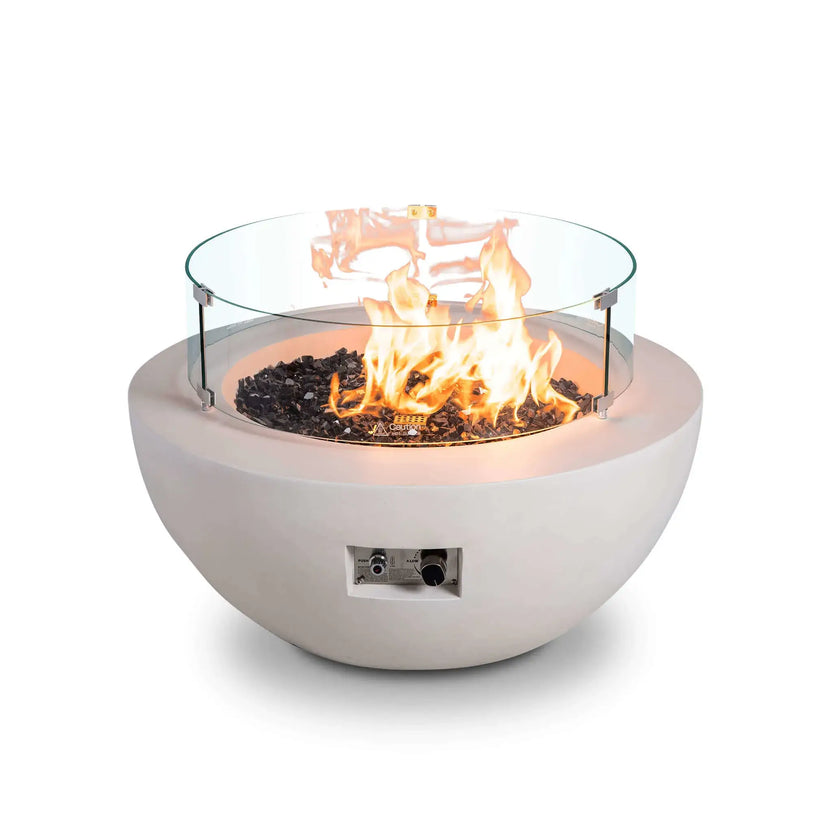 The Flame Havens Refuge Series 36-inch Round Natural Gas White GFRC Concrete Fire Pit is shown operating with the optional tempered glass wind guard installed. Bright flames burn above black reflective tempered fire glass while the clear wind guard enhances flame stability, safety, and visibility without obstructing the contemporary design.