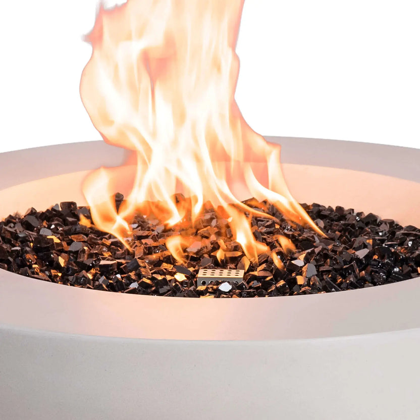 Close-up of the Flame Havens Refuge Series 36-inch Round Natural Gas White GFRC Concrete Fire Pit showcasing bright flames dancing above premium black reflective tempered fire glass. The image highlights the stainless steel CSA ignition system, reflective fire media, and realistic flame pattern that delivers warmth and visual appeal to luxury outdoor spaces.