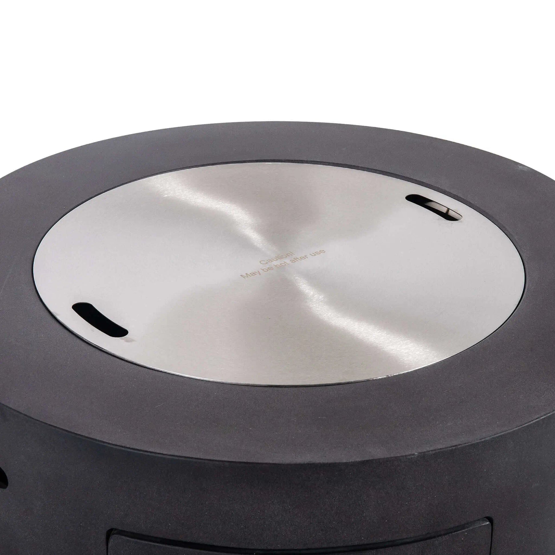 Flame Havens Refuge Series 36-inch Round Propane Gas GFRC Concrete Fire Pit in Graphite Black featuring the optional Stainless Steel Burner Cover installed flush within the burner opening. The brushed stainless steel cover transforms the fire pit into a functional tabletop while protecting the burner from weather, debris, and moisture when the fire feature is not in use.