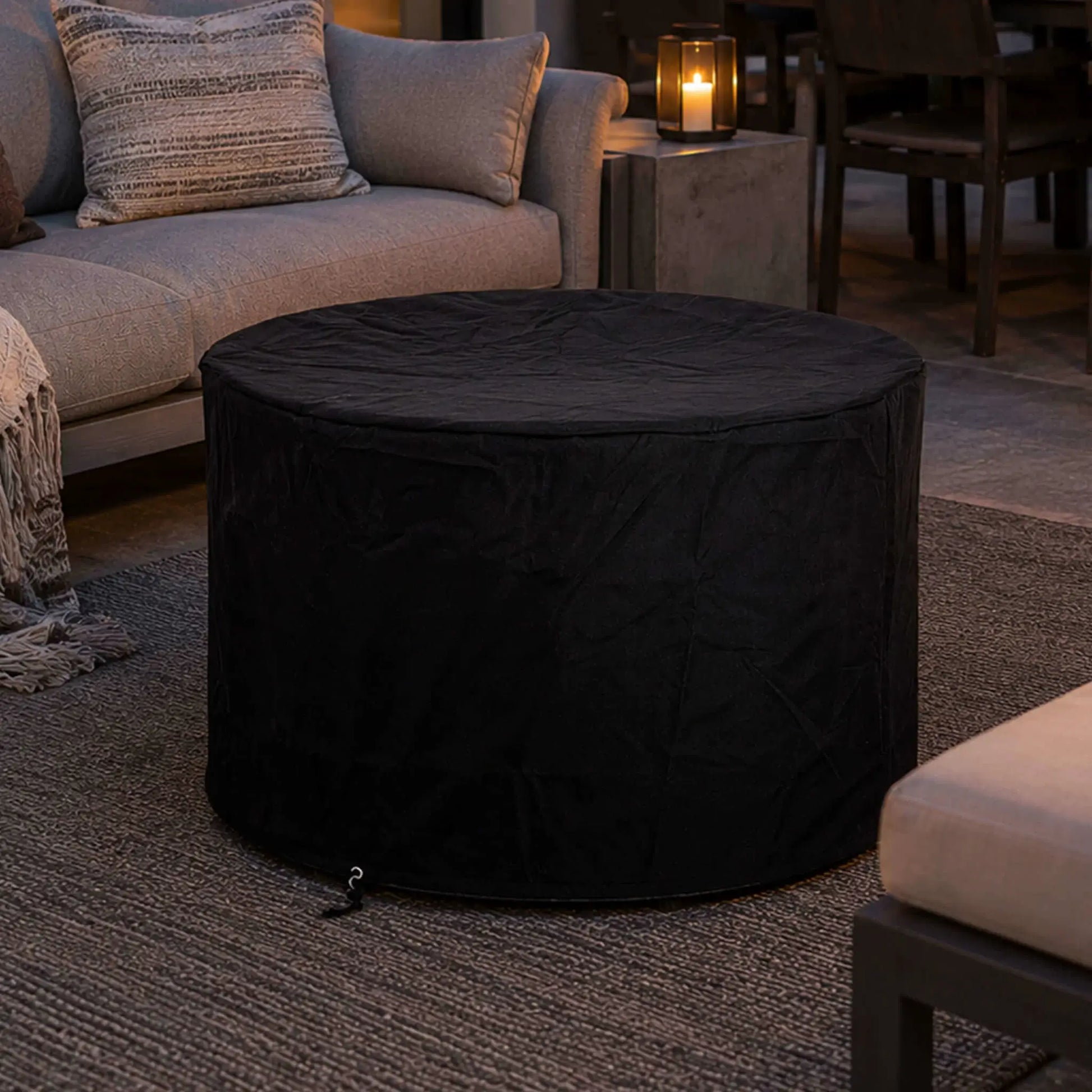 Lifestyle image of the Flame Havens Refuge Series 36-inch Round Propane Gas GFRC Concrete Fire Pit in Natural Gray protected with the fitted black canvas fabric cover. Positioned within a luxury outdoor seating area, the image demonstrates how the weather-resistant cover preserves the fire pit's appearance while complementing upscale patios and backyard entertainment spaces.