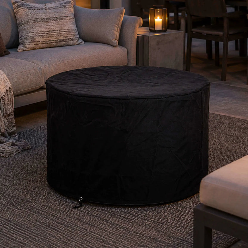 Lifestyle image of the Flame Havens Refuge Series 36-inch Round Propane Gas GFRC Concrete Fire Pit in Natural Gray protected with the fitted black canvas fabric cover. Positioned within a luxury outdoor seating area, the image demonstrates how the weather-resistant cover preserves the fire pit's appearance while complementing upscale patios and backyard entertainment spaces.
