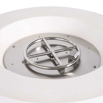 Close-up of the stainless steel burner assembly and CSA-certified ignition system inside the Flame Havens Refuge Series 36-inch Round Propane Gas GFRC Concrete Fire Pit in Ivory White. The exposed circular burner ring, precision gas ports, and ignition components demonstrate the premium engineering and durable stainless steel construction beneath the fire media.