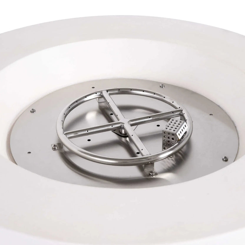 Close-up of the stainless steel burner assembly and CSA-certified ignition system inside the Flame Havens Refuge Series 36-inch Round Propane Gas GFRC Concrete Fire Pit in Ivory White. The exposed circular burner ring, precision gas ports, and ignition components demonstrate the premium engineering and durable stainless steel construction beneath the fire media.