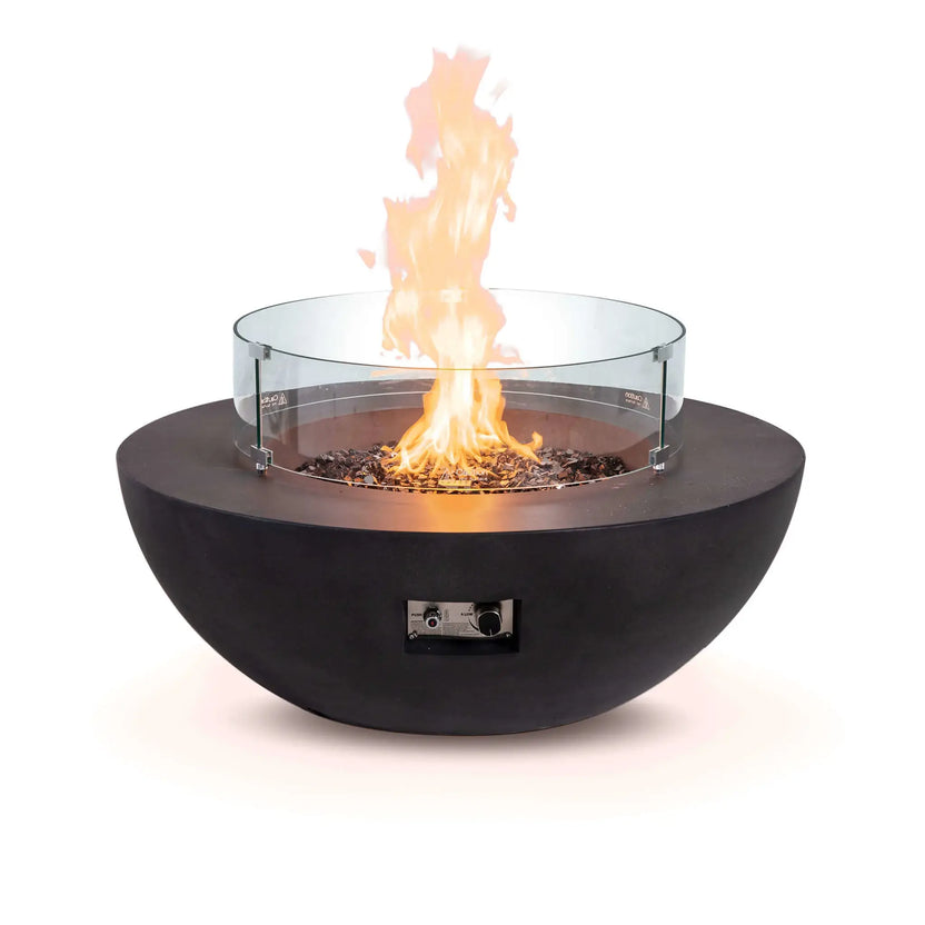 The Flame Havens Refuge Series 43-inch Round Natural Gas Black GFRC Concrete Fire Pit operating with reflective tempered black fire glass and a clear tempered glass wind guard installed. The wind guard surrounds the flame while maintaining visibility and helping improve flame stability in breezy outdoor environments.