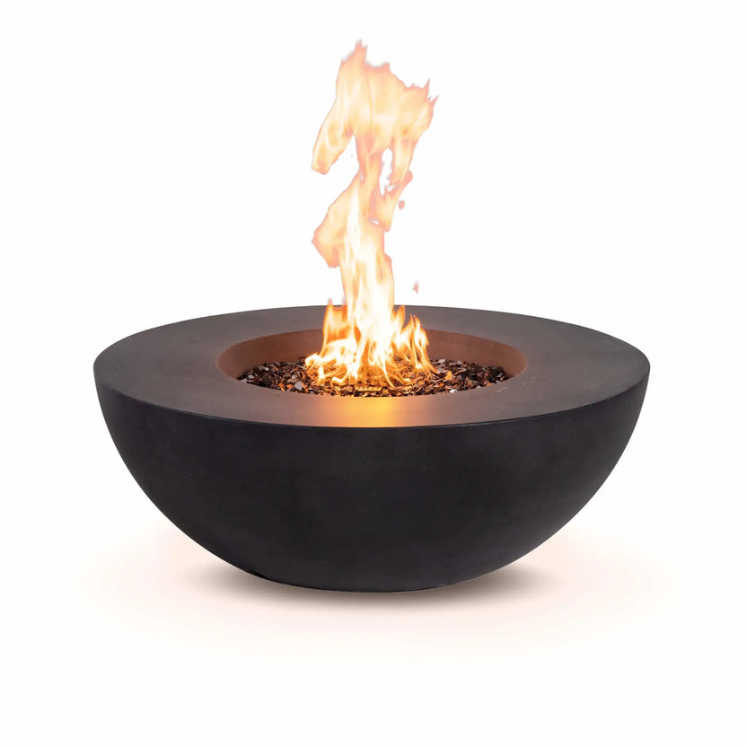 Lifestyle image of the Flame Havens Refuge Series 43-inch Round Natural Gas Black GFRC Concrete Fire Pit featuring reflective tempered black fire glass and a tempered glass wind guard. Set within a luxurious outdoor seating area at dusk, the glowing fire creates a warm, inviting atmosphere for entertaining and relaxing.