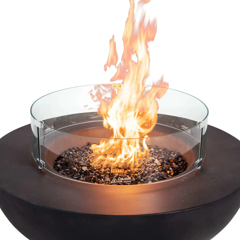 Front view of the Flame Havens Refuge Series 43-inch Round Natural Gas Black GFRC Concrete Fire Pit featuring reflective tempered black fire glass, a clear tempered glass wind guard, and a vibrant flame. The premium wind guard surrounds the burner to improve flame stability while preserving an open view of the fire, creating a refined centerpiece for luxury outdoor living spaces.
