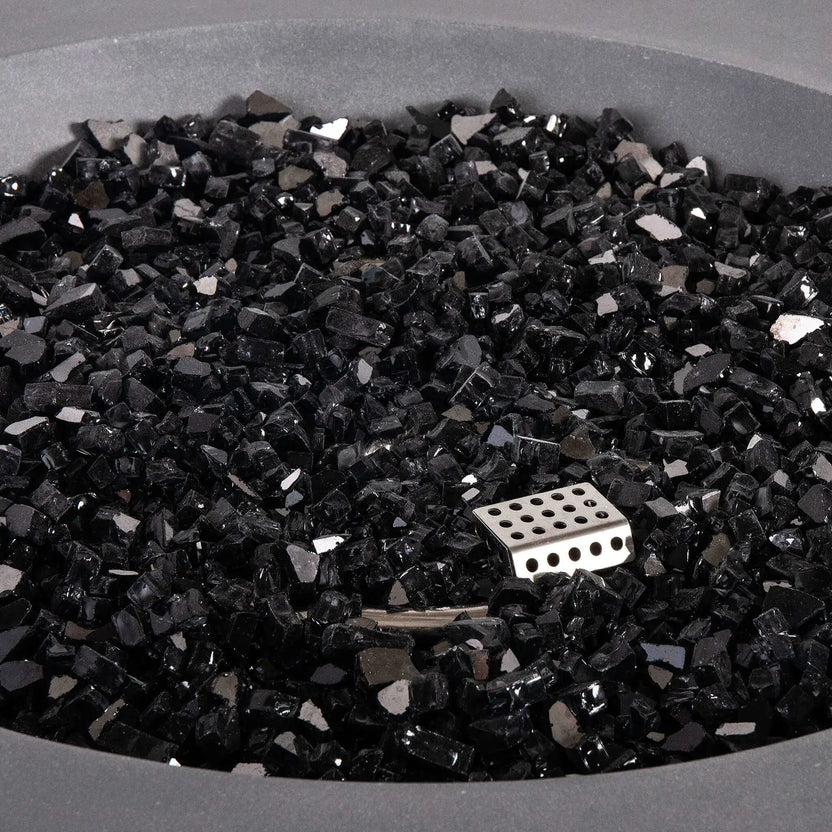 Close-up of the reflective tempered black fire glass inside the Flame Havens Refuge Series 43-inch Round Natural Gas Gray GFRC Concrete Fire Pit. The premium fire media surrounds the concealed burner and ignition components, creating a polished appearance while maximizing flame reflection and visual depth.