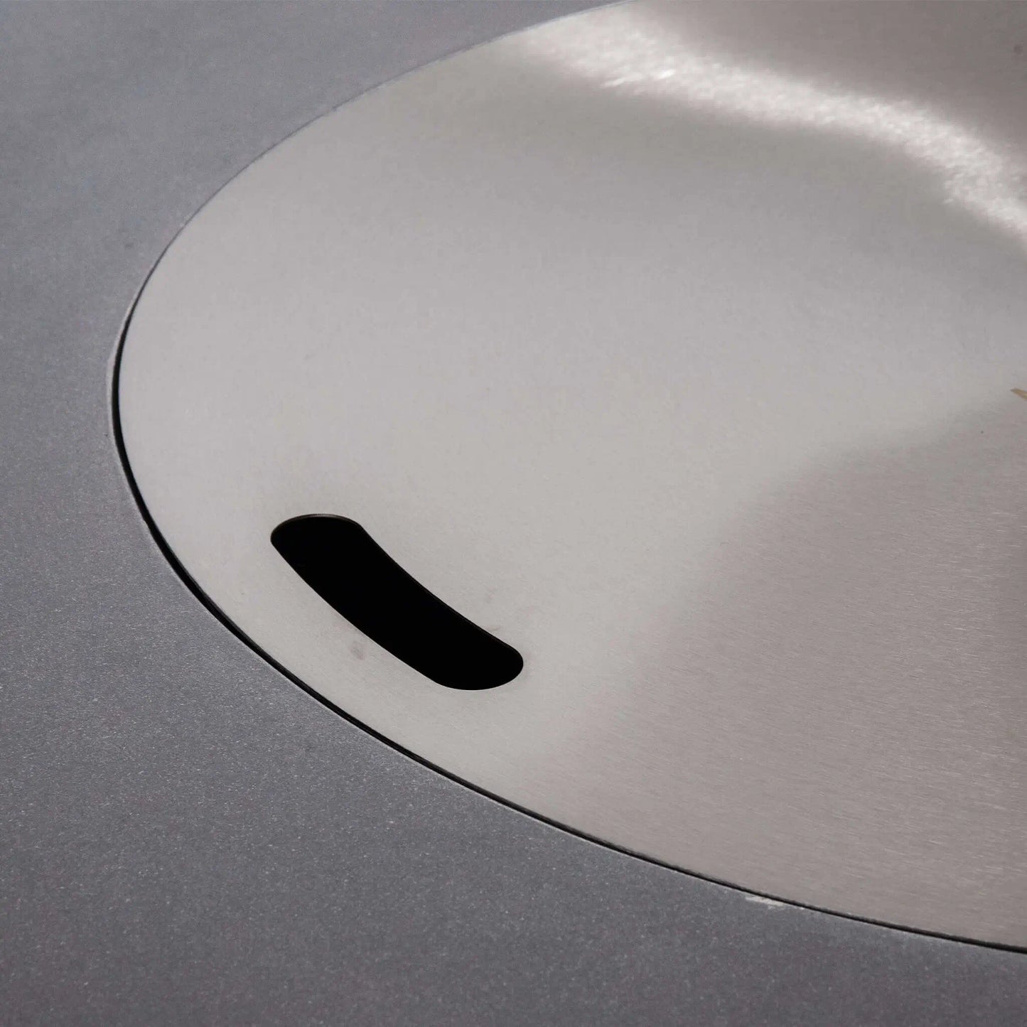 Close-up of the stainless steel burner cover installed on the Flame Havens Refuge Series 43-inch Round Natural Gas Gray GFRC Concrete Fire Pit. The precision-fitted cover conceals the burner opening, transforming the fire pit into a sleek tabletop surface when the fire feature is not in operation.