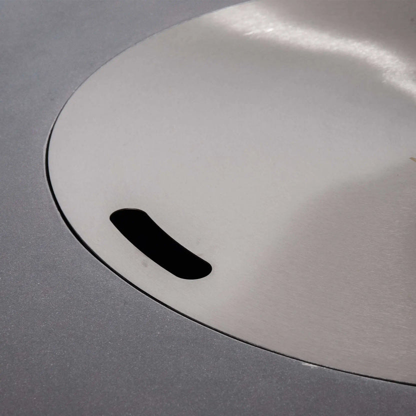 Close-up of the stainless steel burner cover installed on the Flame Havens Refuge Series 43-inch Round Natural Gas Gray GFRC Concrete Fire Pit. The precision-fitted cover conceals the burner opening, transforming the fire pit into a sleek tabletop surface when the fire feature is not in operation.