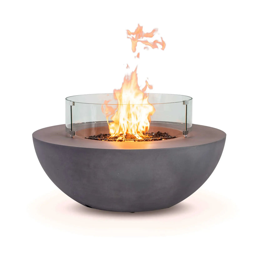 Front view of the Flame Havens Refuge Series 43-inch Round Natural Gas Gray GFRC Concrete Fire Pit featuring reflective tempered black fire glass, an active natural gas flame, and a clear tempered glass wind guard. The premium wind guard improves flame stability while preserving an unobstructed view, adding both safety and sophistication to the outdoor fire feature.