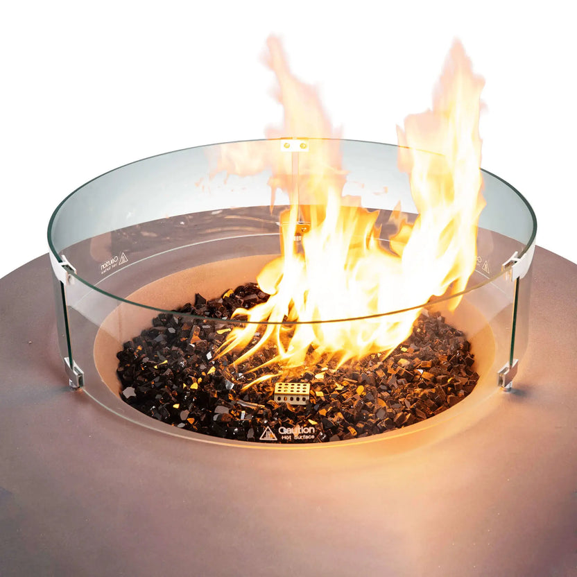 Close-up of the Flame Havens Refuge Series 43-inch Round Natural Gas Gray GFRC Concrete Fire Pit featuring reflective tempered black fire glass, a clear tempered glass wind guard, and a bright natural gas flame. The circular wind guard protects the flame while maintaining an open view of the fire for safe outdoor enjoyment.