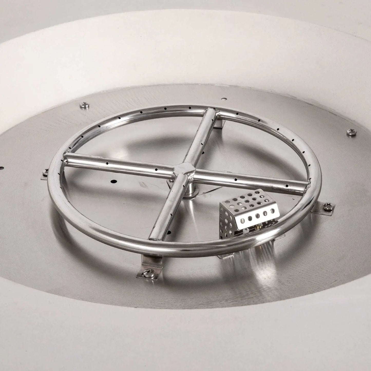 Close-up of the Flame Havens Refuge Series 43-inch Round Natural Gas White GFRC Concrete Fire Pit showing the stainless steel burner ring, CSA-certified ignition system, and ignition hood installed inside the stainless burner pan. This detailed view highlights the premium internal components before black fire glass is added.