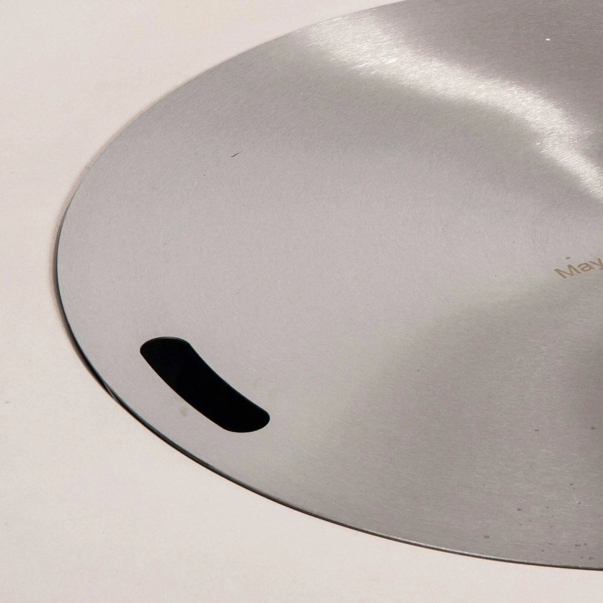 Detailed close-up of the stainless steel burner cover designed for the Flame Havens Refuge Series 43-inch Round Natural Gas White GFRC Concrete Fire Pit. The brushed stainless cover sits flush within the burner opening and features integrated hand slots for easy removal while protecting the burner when the fire pit is not in use.