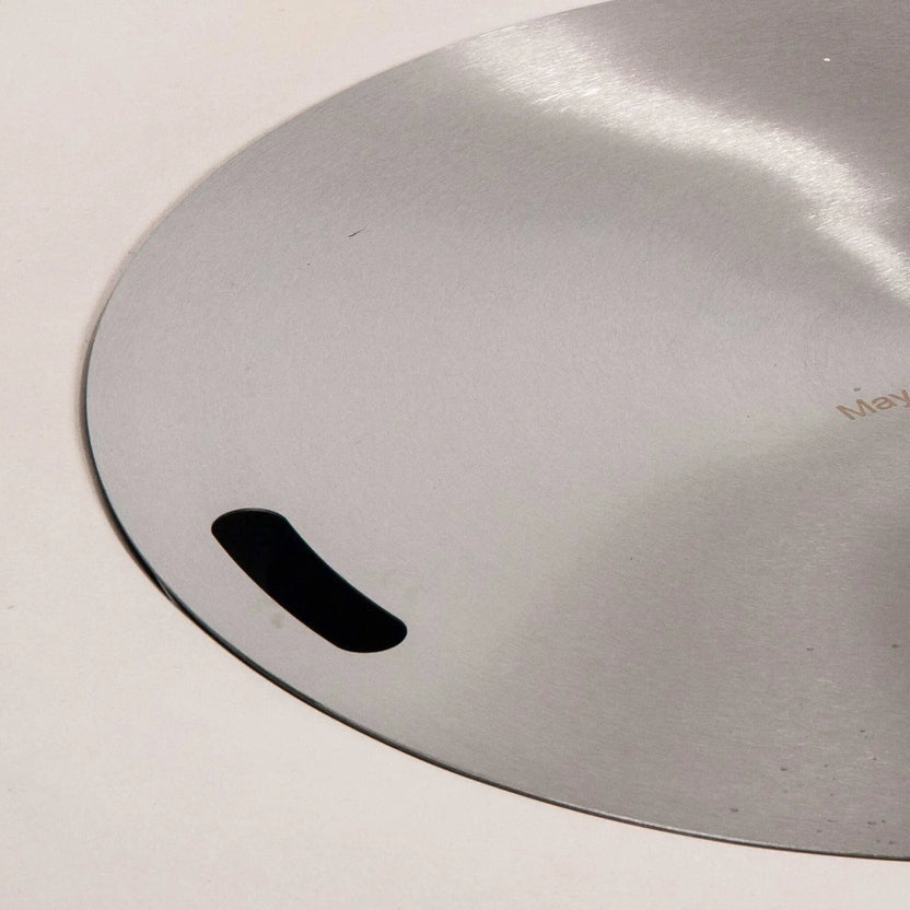 Detailed close-up of the stainless steel burner cover designed for the Flame Havens Refuge Series 43-inch Round Natural Gas White GFRC Concrete Fire Pit. The brushed stainless cover sits flush within the burner opening and features integrated hand slots for easy removal while protecting the burner when the fire pit is not in use.