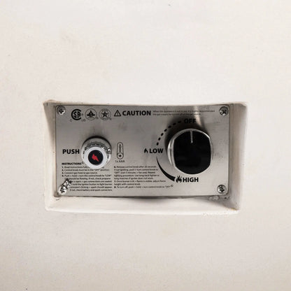 Close-up of the recessed control panel on the Flame Havens Refuge Series 43-inch Round Natural Gas White GFRC Concrete Fire Pit. The image clearly shows the push-button electronic ignition, flame control knob, ignition instructions, and CSA-certified safety labeling integrated into the fire pit's clean exterior.
