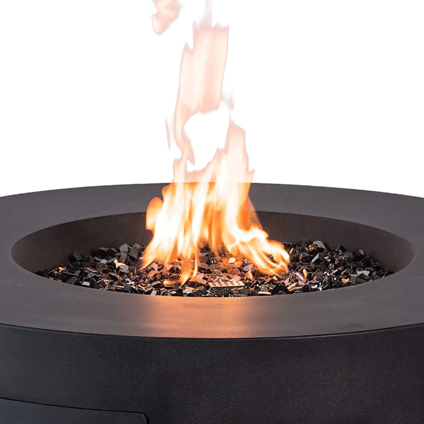 The Flame Havens Refuge Series 43-inch Round Propane Gas GFRC Concrete Fire Pit in Black operating with a vibrant natural flame rising from black reflective fire glass. This close-up showcases the stainless steel burner, CSA ignition system, and smooth black GFRC concrete construction, highlighting the premium performance and modern outdoor entertaining appeal of this luxury propane fire pit.