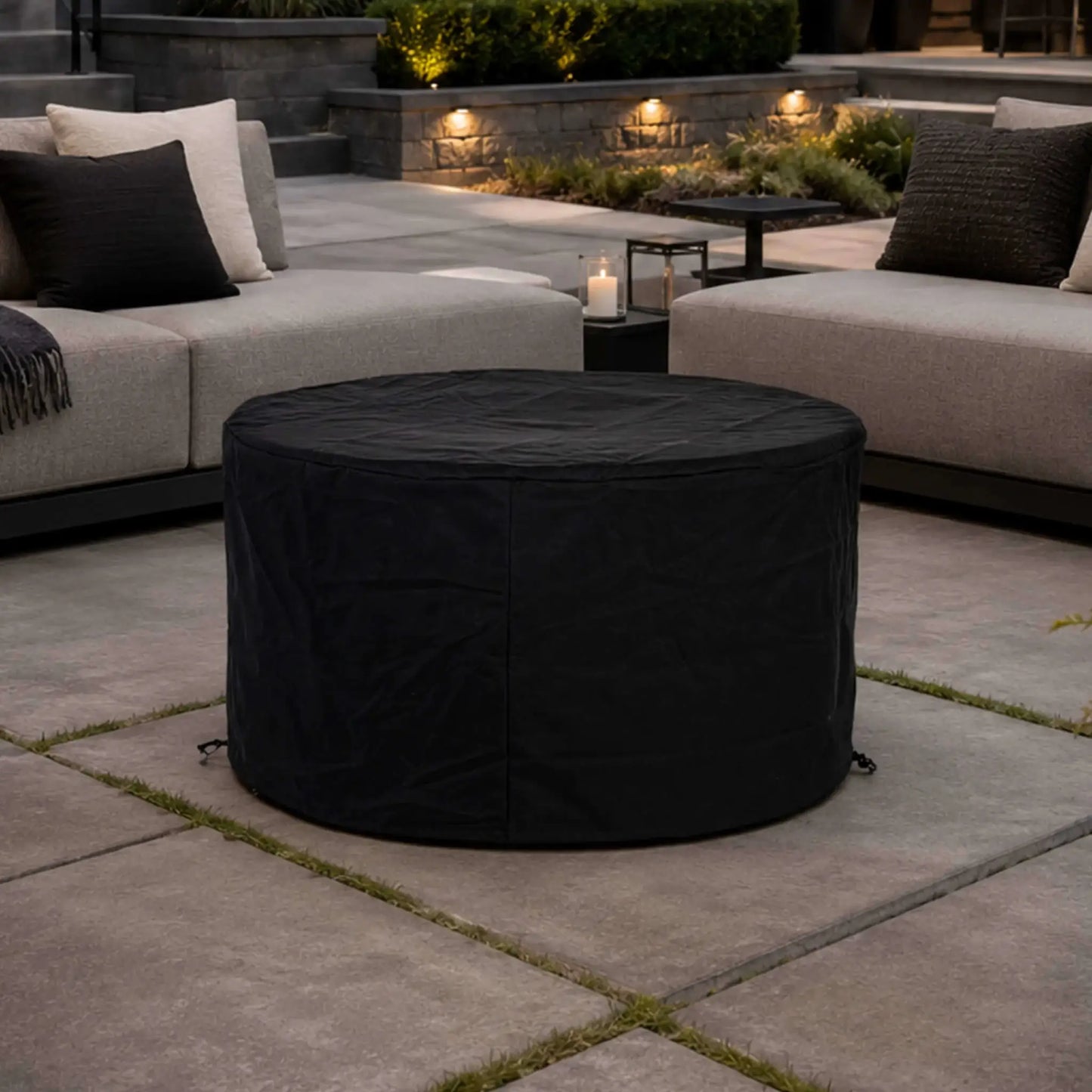 The Flame Havens Refuge Series 43-inch Round Propane Gas GFRC Concrete Fire Pit protected with its black canvas fabric cover in a luxury backyard patio setting. Positioned between modern outdoor lounge seating, the fitted cover demonstrates year-round weather protection while blending seamlessly into an upscale outdoor living environment.