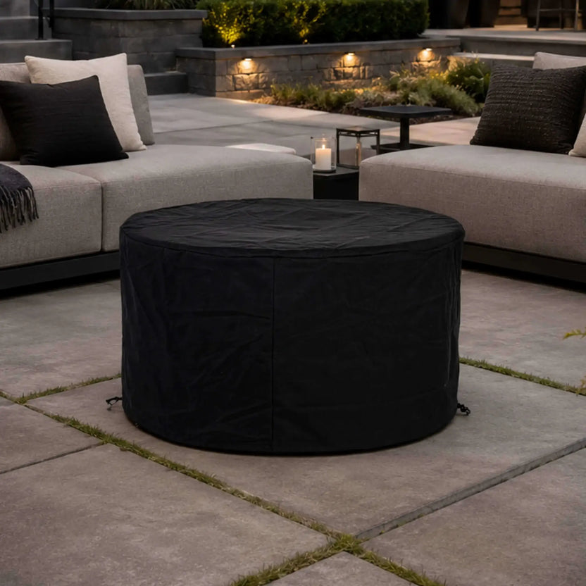 The Flame Havens Refuge Series 43-inch Round Propane Gas GFRC Concrete Fire Pit protected with its black canvas fabric cover in a luxury backyard patio setting. Positioned between modern outdoor lounge seating, the fitted cover demonstrates year-round weather protection while blending seamlessly into an upscale outdoor living environment.
