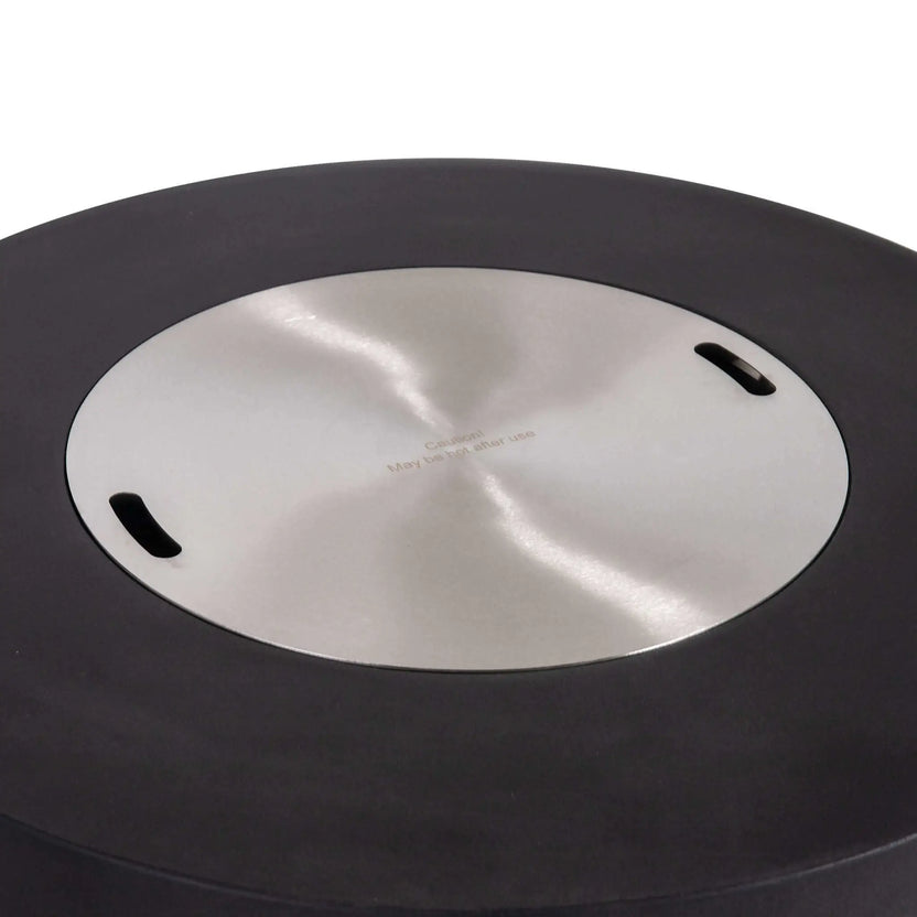 The Flame Havens Refuge Series 43-inch Round Propane Gas GFRC Concrete Fire Pit in Black featuring the optional stainless steel burner cover installed. The brushed stainless cover fits flush within the recessed burner opening, transforming the fire pit into a functional tabletop while protecting the burner. The image highlights the premium black GFRC concrete finish and clean, contemporary outdoor design.