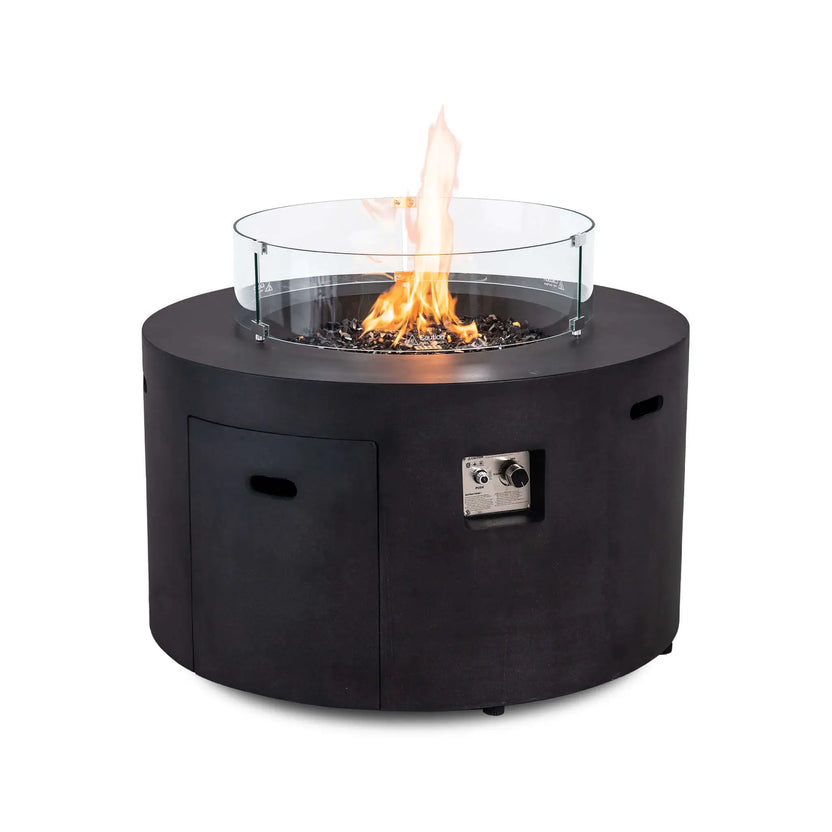 The Flame Havens Refuge Series 43-inch Round Propane Gas GFRC Concrete Fire Pit in Black burning with the optional tempered glass wind guard installed. The clear glass guard surrounds the vibrant flame above black reflective fire glass, enhancing flame stability while preserving unobstructed views of this luxury outdoor propane fire feature.