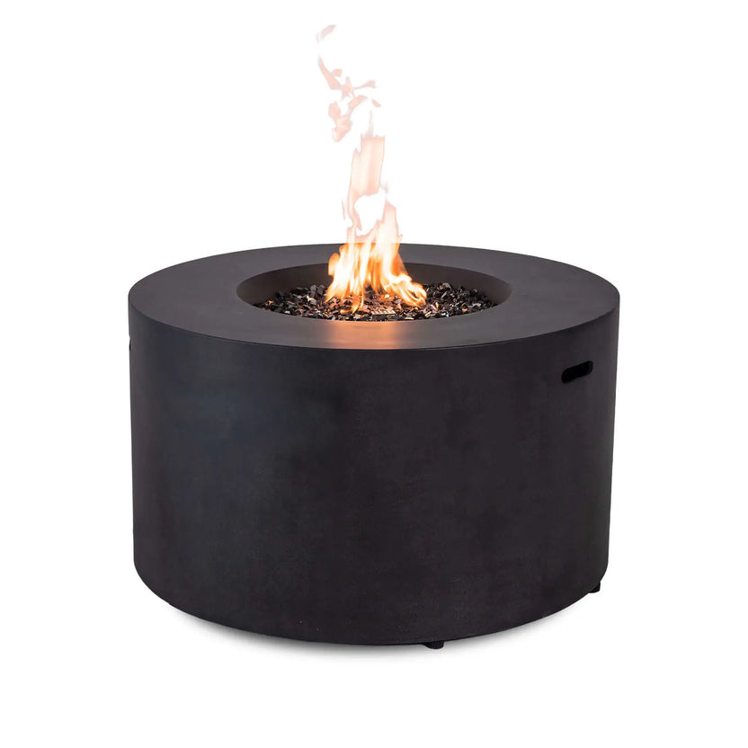 The Flame Havens Refuge Series 43-inch Round Propane Gas GFRC Concrete Fire Pit in Black operating with a vibrant flame rising above premium black reflective fire glass. Captured from the rear without the control panel visible, the image emphasizes the clean cylindrical GFRC concrete design and impressive propane fire presentation.