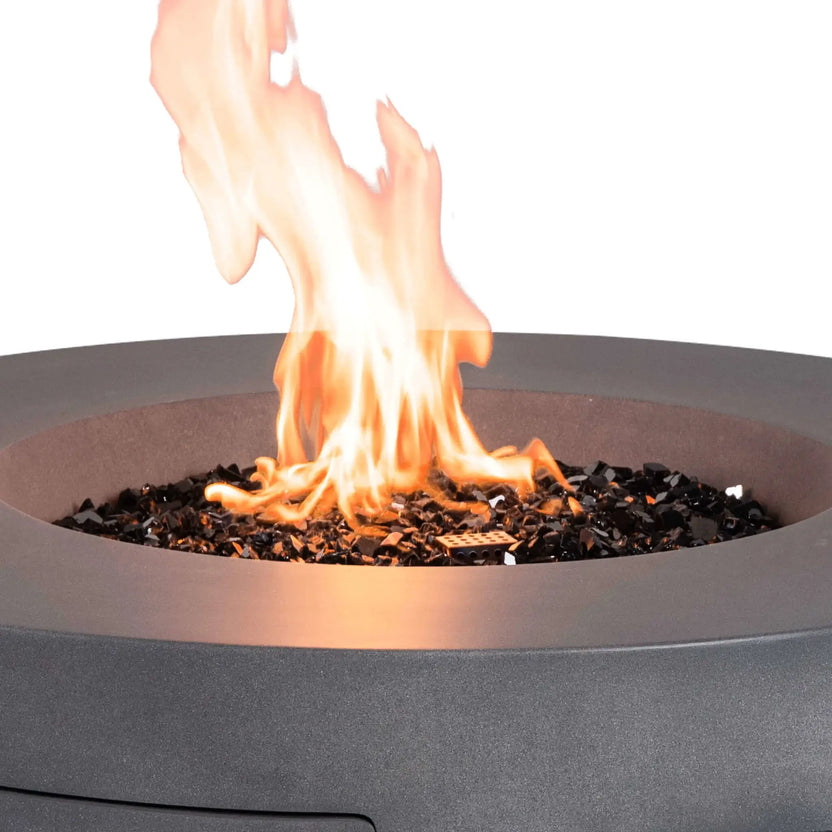 The Flame Havens Refuge Series 43-inch Round Propane Gas GFRC Concrete Fire Pit in Gray with a vibrant propane flame rising through premium black reflective fire glass. This close-up emphasizes the realistic flame pattern, recessed burner design, durable GFRC concrete construction, and luxurious outdoor ambiance created by the fire feature.